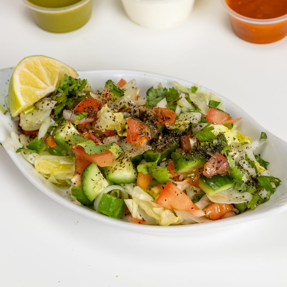 Fresh Afghan salad with chopped lettuce, tomatoes, cucumbers, onions, and herbs, garnished with a lime wedge.