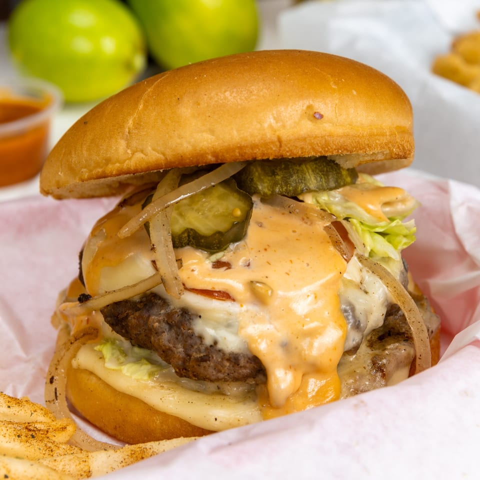 A Halal Kitchen Cafe burger with melted cheese, onions, pickles, and special sauce, with fries.