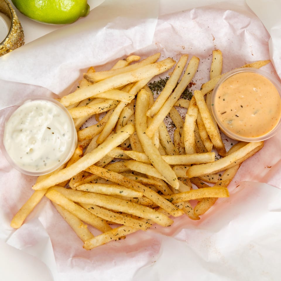 Seasoned fries with two dipping sauces, one white and one orange, in a paper-lined basket.