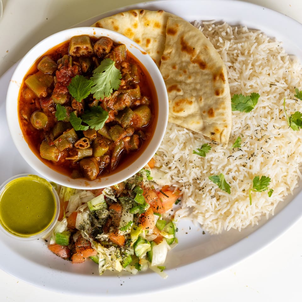 Afghan okra stew with rice, naan, and salad, served on a white plate at Halal Kitchen Cafe.