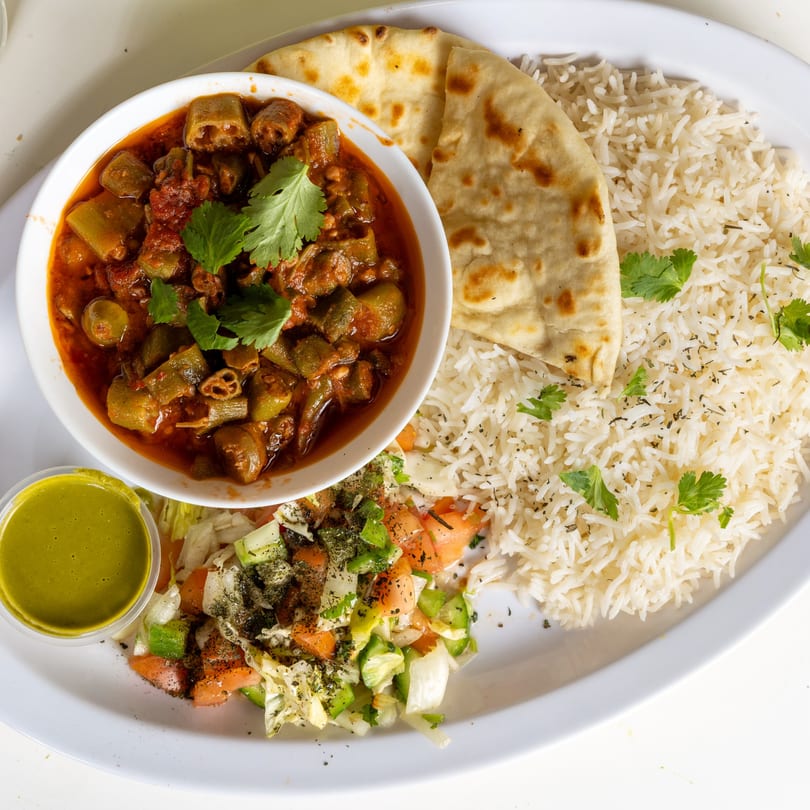 Afghan okra stew with rice, naan, and salad, served on a white plate at Halal Kitchen Cafe.