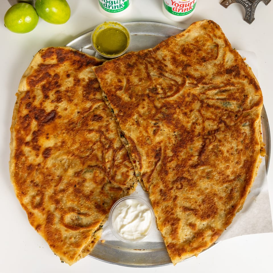 Two golden-brown Afghan Bolani flatbreads, with green and white dipping sauces, and two yogurt drinks.