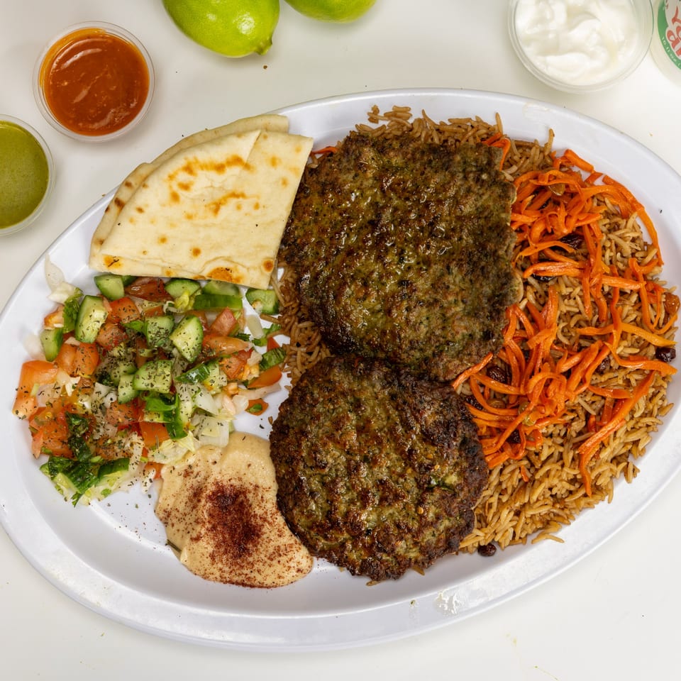 Two Afghan beef patties with rice, carrots, salad, hummus, and naan on a white plate.