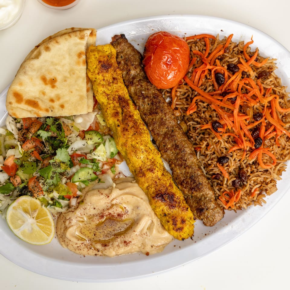 Halal Kitchen Cafe's Afghan platter with two kebabs, rice, salad, hummus, naan, and a lemon.