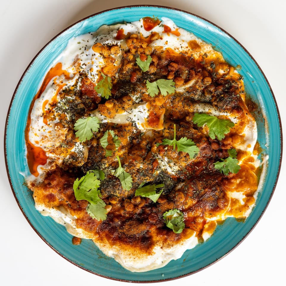 Afghan Mantu dumplings topped with yogurt, spiced meat sauce, chickpeas, and fresh cilantro on a blue plate.